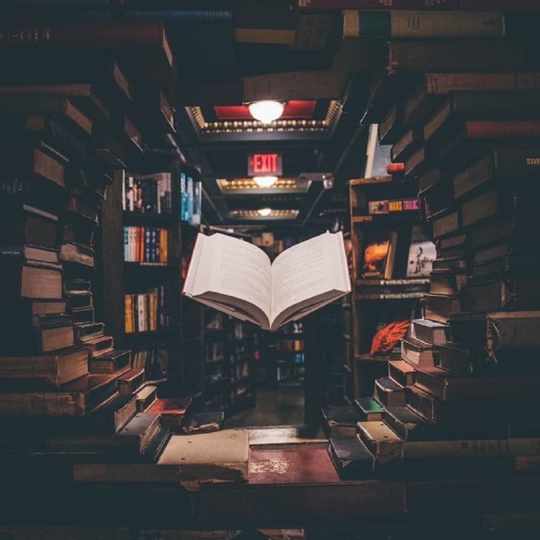 A floating open book, surrounded by stacks of other books