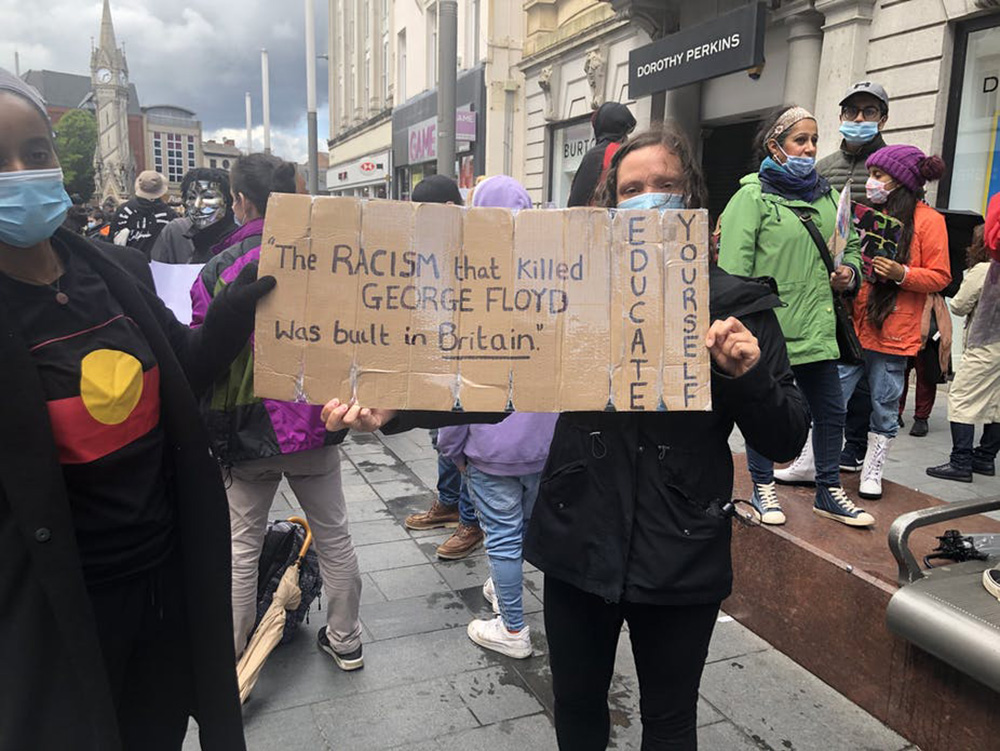 A protest sign: The RACISM that killed GEORGE FLOYD was built in Britain. Educate yourself.
