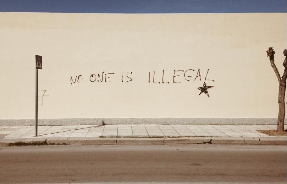 A wall with graffiti that reads 'no one is illegal'